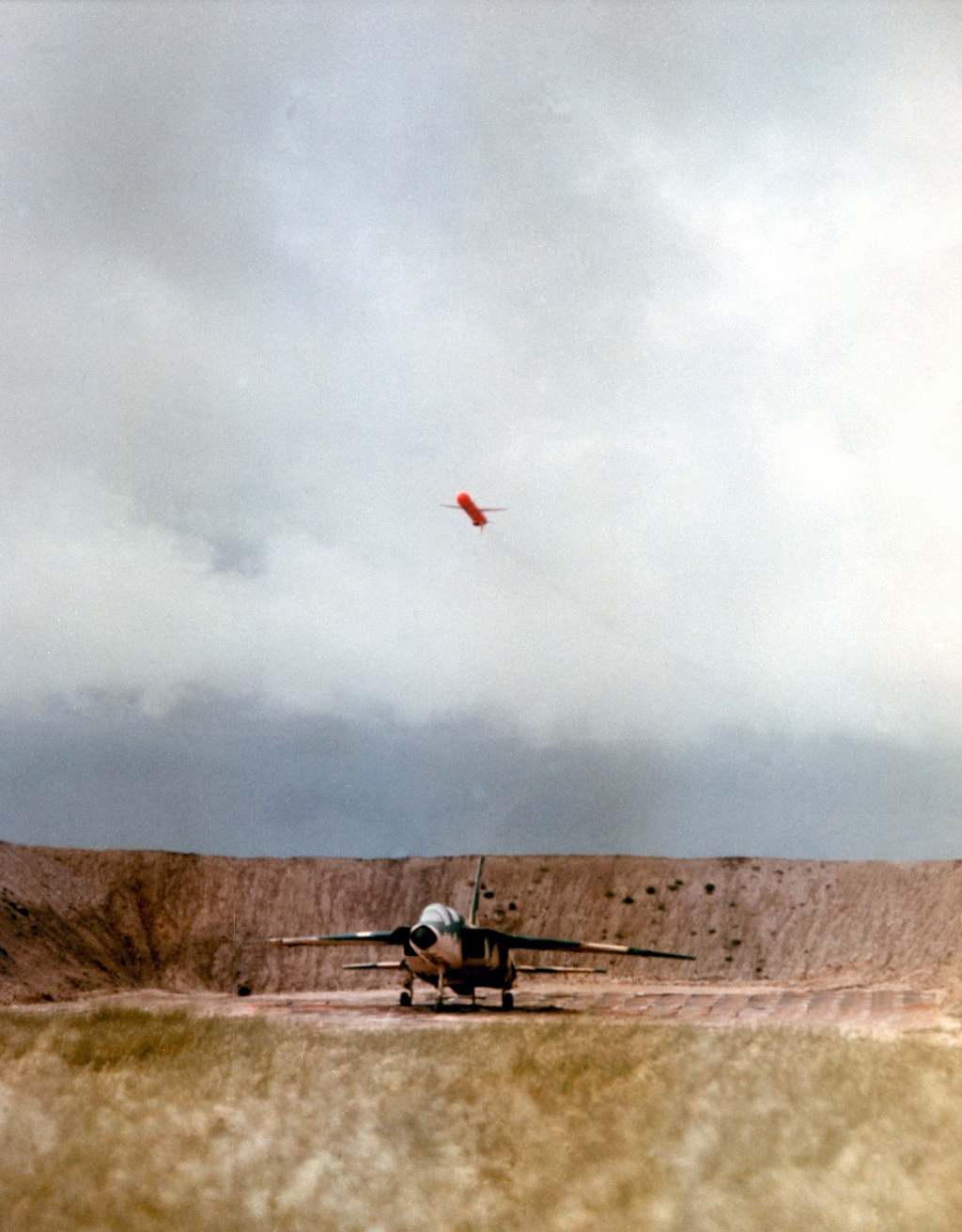 6a. Launched from a submerged United States Navy submarine off the coast of California and traveling more than 400 miles, the BGM-109 Tomahawk cruise missile approaches the target,a revetted aircraft, April 1, 1986, San Clemente Island, State of California, USA. Photo Credit: Defense Visual Information Center (DVIC, http://www.DoDMedia.osd.mil, DN-SC-86-06113) and United States Navy (USN, http://www.navy.mil), United States Department of Defense (DoD, http://www.DefenseLink.mil or http://www.dod.gov), Government of the United States of America (USA).