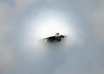 Transonic F-14D Tomcat Fighter Jet With Its Prandtl-Glauert Cloud on July 28, 2006, USS Theodore Roosevelt (CVN 71) Atlantic Ocean. The United States Navy F-14D Tomcat figher jet is 'aircraft number 100, assigned to the Tomcatters of Fighter Squadron Three One (VF-31),' and is making a 'near supersonic fly-by above the flight deck of USS Theodore Roosevelt (CVN 71).' Source for the quotes: 'F-14 near supersonic fly-by' at <http://www.navy.mil/view_single.asp?id=37555>). Photo Credit: Mass Communication Specialist 3rd Class Nathan Laird, Navy NewsStand - Eye on the Fleet Photo Gallery (http://www.news.navy.mil/view_photos.asp, 060728-N-7241L-026), United States Navy (USN, http://www.navy.mil), United States Department of Defense (DoD, http://www.DefenseLink.mil or http://www.dod.gov), Government of the United States of America (USA). This picture (photograph) is included in 'ChamorroBible.org: Prandtl-Glauert Condensation Clouds, 1st Collection', ChamorroBible.org, Manguaguan na Palabran Si Yuus -- God's Precious Words of August 17, 2004.