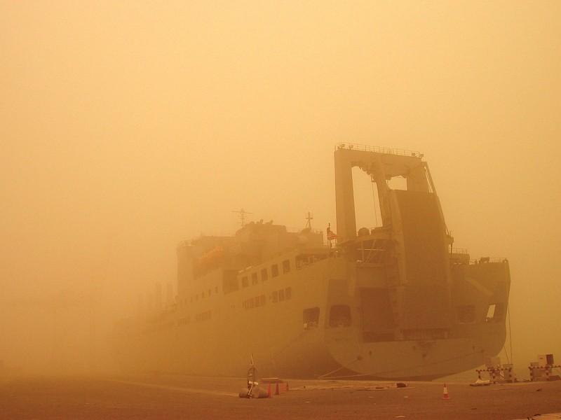 8. USNS Brittin (T-AKR 305) is a United States Navy Military Sealift Command Large, Medium-Speed Roll-on/Roll-off Ship (LMSR), But This Windstorm Generates a Sandstorm That Is So Huge It Significantly Blocks (Filters) the Sun's Rays -- Casting a Yellow-Orange Hue Everywhere -- and Dramatically Obscures Much of the Docked Ship, 2003, Port of Ash Shuaybah, Dawlat al Kuwayt - State of Kuwait. Photo Credit: Military Sealift Command: 2003 in Review (http://www.msc.navy.mil/annualreport/2003/organization.htm) and Sealift, May 2003: 'MSC ships, crews deliver to inhospitable places' (http://www.msc.navy.mil/sealift/2003/May/inhospitable.htm), Military Sealift Command (MSC, http://www.msc.navy.mil), United States Navy (USN, http://www.navy.mil), United States Department of Defense (DoD, http://www.DefenseLink.mil or http://www.dod.gov), Government of the United States of America (USA).