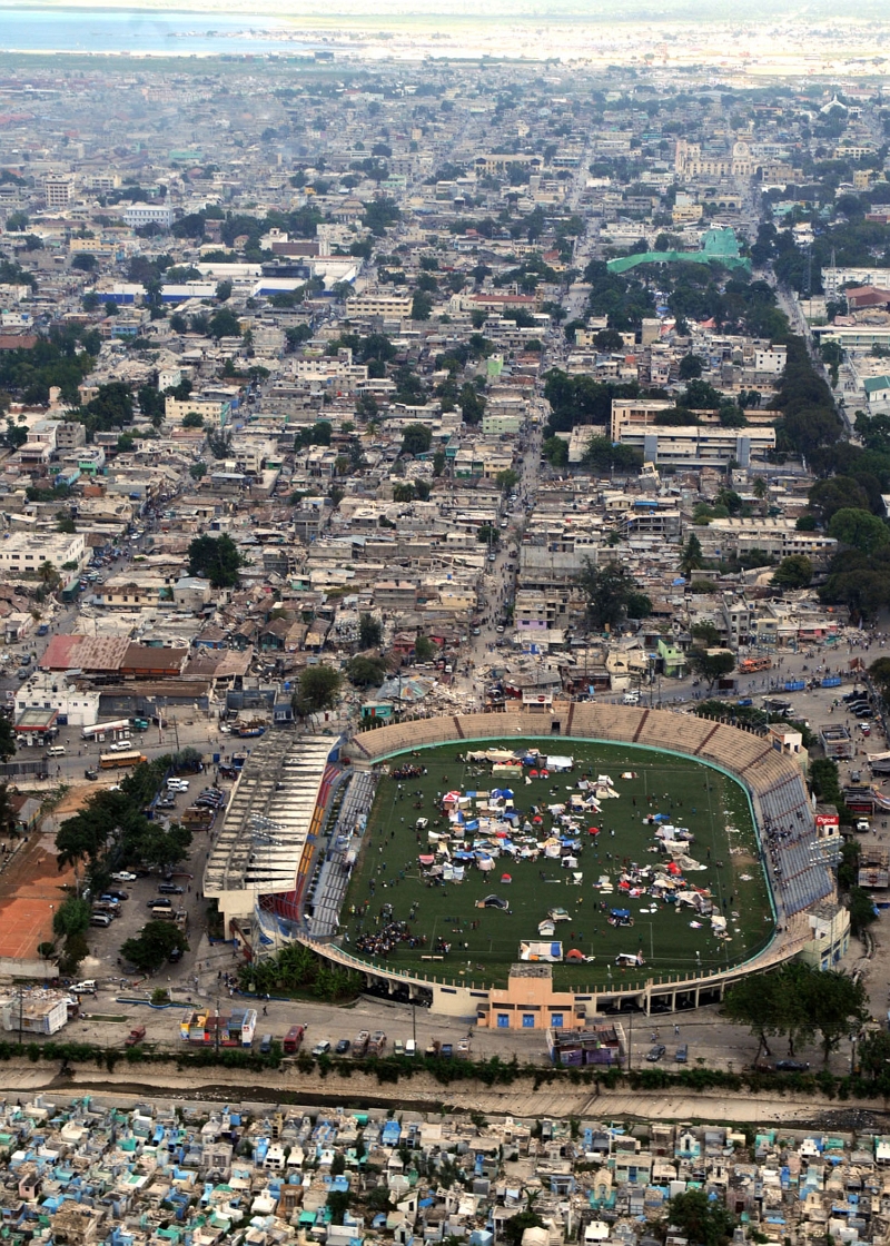 34. Earthquake Survivors (Refugees) and Their Makeshift Shelters Inside the Soccer (Football) Stadium -- Backdropped By the Earthquake-Damaged City of Port-au-Prince, January 17, 2010, Republique d'Haiti (Repiblik d' Ayiti) - Republic of Haiti. Photo Credit: Mass Communication Specialist 2nd Class Joel Carlson, United States Navy; Defense Visual Information (DVI, http://www.DefenseImagery.mil, 100117-N-4275C-190) and United States Navy (USN, http://www.navy.mil), United States Department of Defense (DoD, http://www.DefenseLink.mil or http://www.dod.gov), Government of the United States of America (USA).